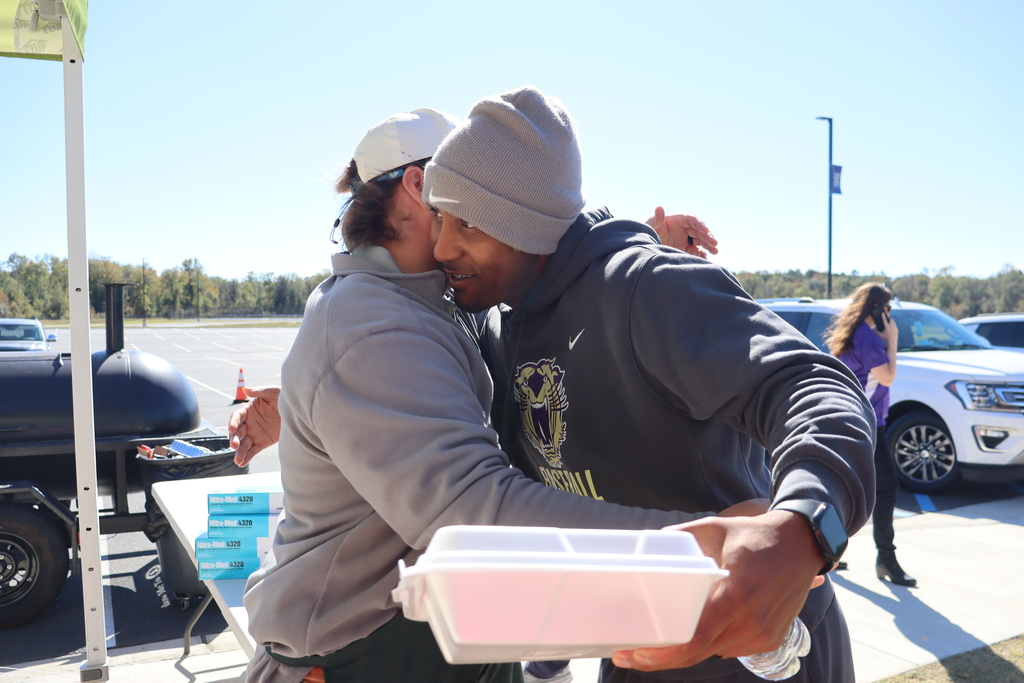 Two men share a friendly hug while one holds a boxed meal.