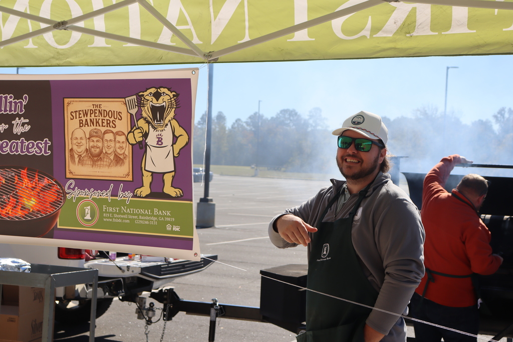 A First National Bank volunteer smiles under the tent beside a Grillin’ for the Greatest event banner.