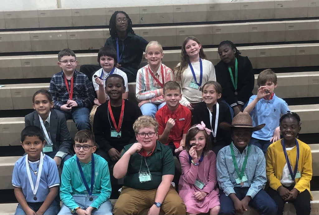 A group of elementary school students sitting on bleachers, smiling and wearing medals around their necks.
