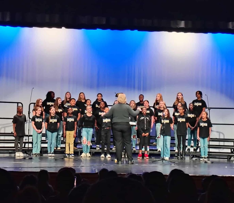 7th grade chorus students standing on stage with a blue and white lighting effect behind them.