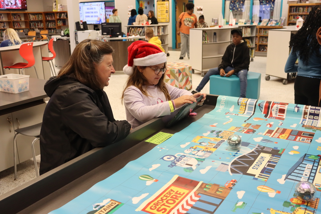 Child in a Santa hat programs a small robot on a colorful city-themed mat while an adult watches