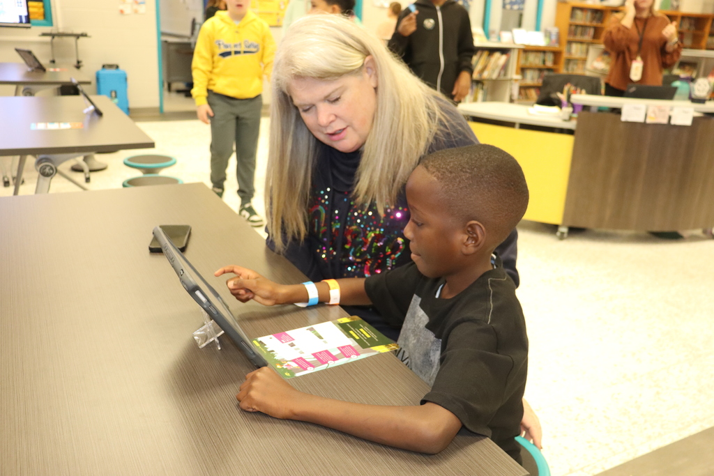Adult assists a student using a tablet during a coding session in a school library.