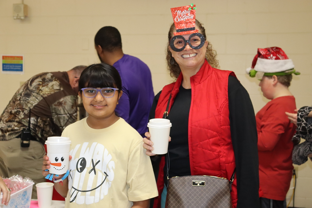 Child and adult hold snowman cups of hot cocoa and smile indoors