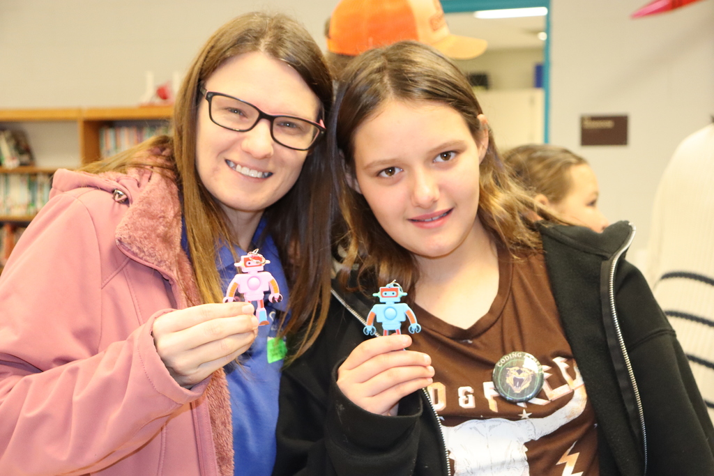 Two people hold up small robot-shaped prizes and smile at the camera.
