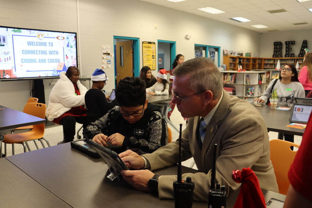 Adult assists a student using a tablet during a coding session in a school library.