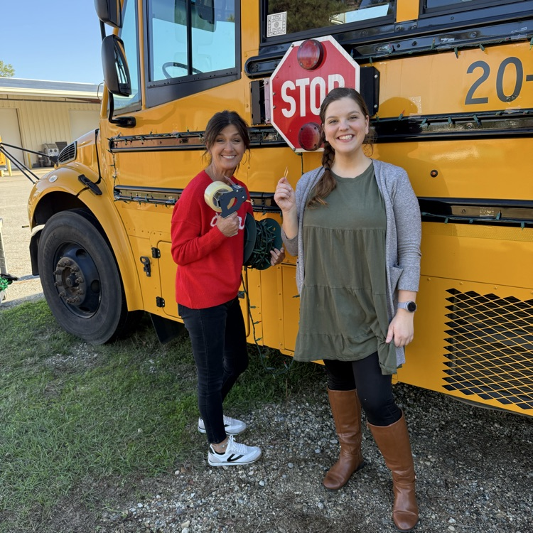 Two women decorate a yellow school bus with Christmas lights in preparation for a holiday parade.