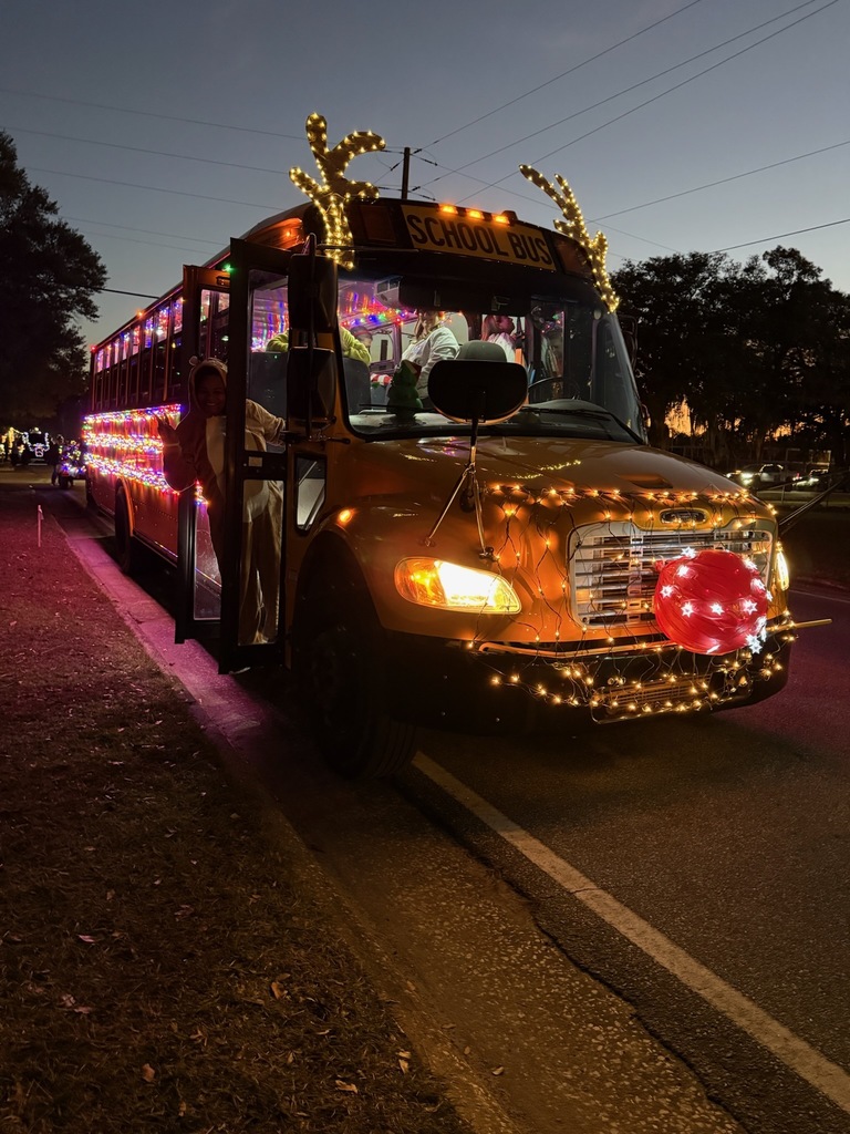 School bus decorated with Christmas lights, reindeer antlers, and a glowing red nose parked at night.
