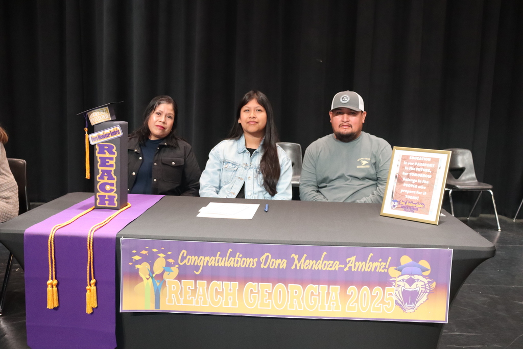 Student seated at a table with family members during a REACH Georgia 2025 scholarship signing ceremony.