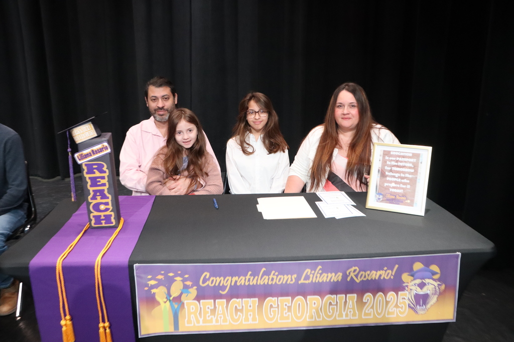 Student seated at a table with family members during a REACH Georgia 2025 scholarship signing ceremony.