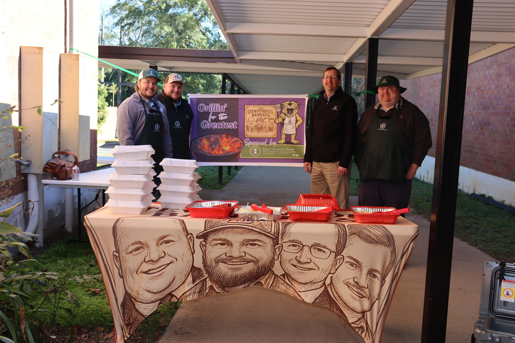 Four First National Bank staff members stand behind a table with food containers and a “Grillin’ for the Greatest” banner, supporting educators at New Beginnings Learning Center.