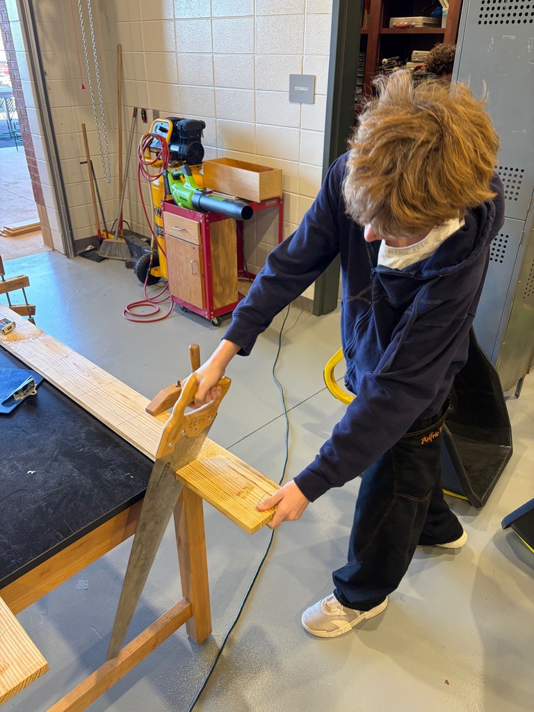 A student using a hand saw to cut a piece of wood.