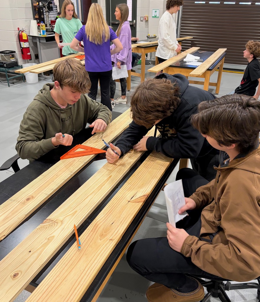 Students collaborating in order to read plans and mark cut places on a board.