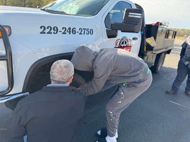 Student helps Jeff Lynn from Delta Tire work on a tire.