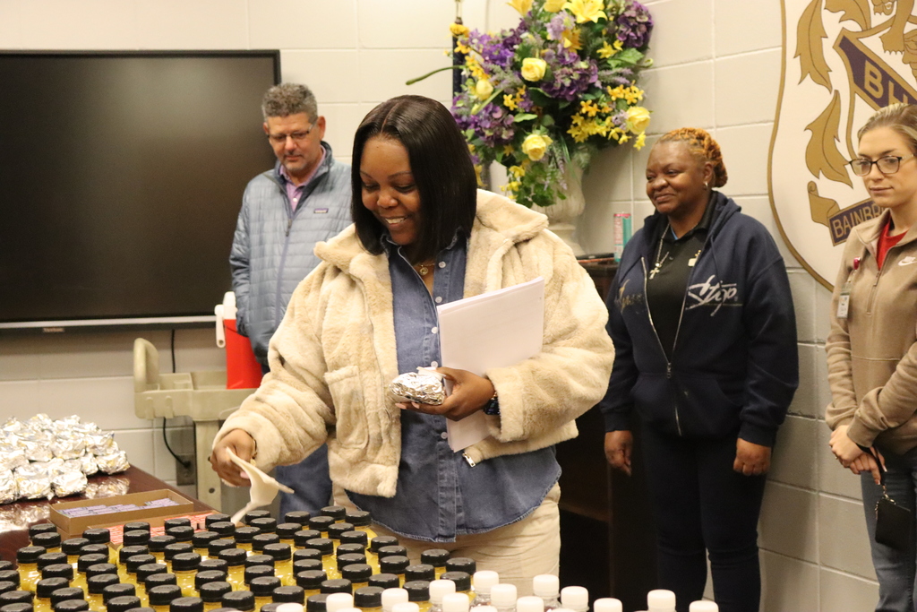 A staff member smiles while selecting breakfast items during a teacher appreciation event as others look on nearby.