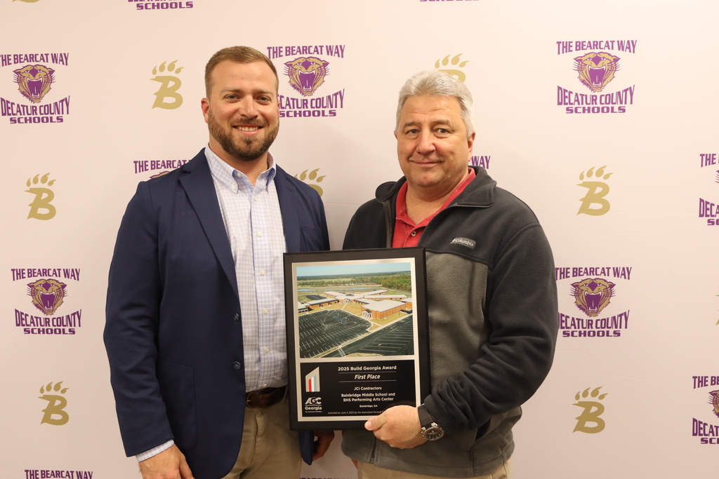 Two men stand in front of a Decatur County Schools backdrop, smiling and holding a framed 2025 Build Georgia Award for Bainbridge Middle School and the Bainbridge High School Performing Arts Center.