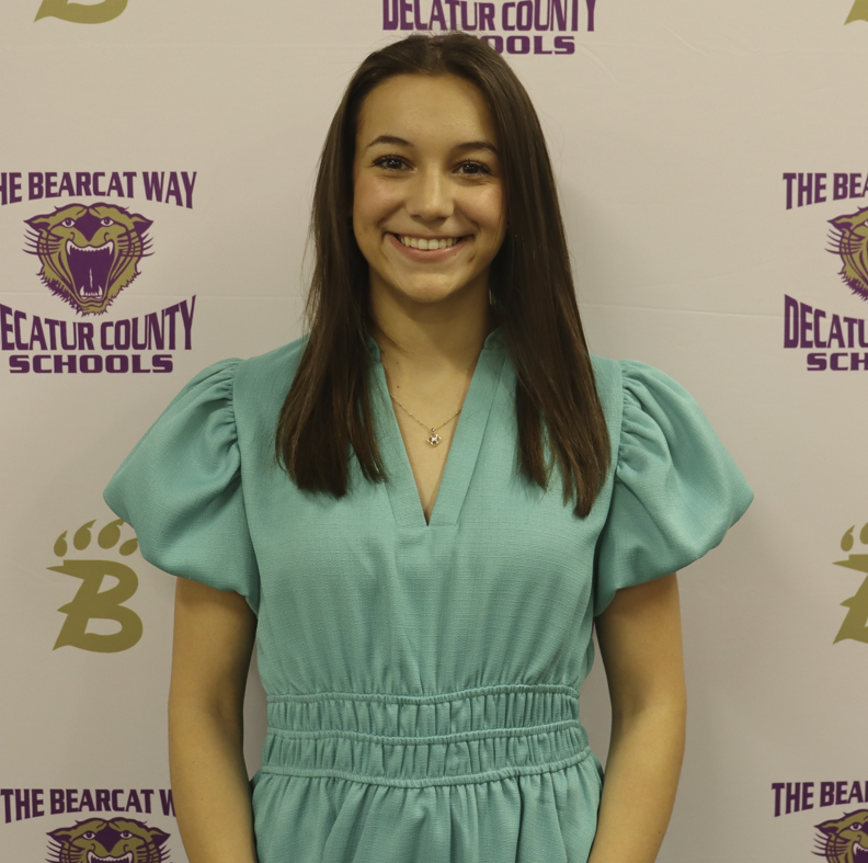 A young women stands in front of a decatur county schools branded media backdrop smiling