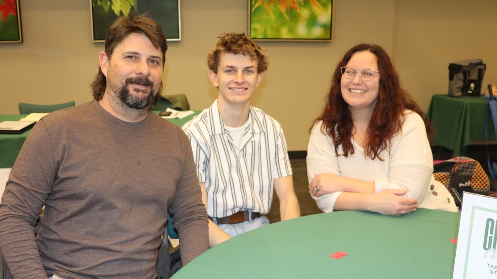Mitchell Carter seated at a table with two adults, all smiling during a recognition luncheon event.