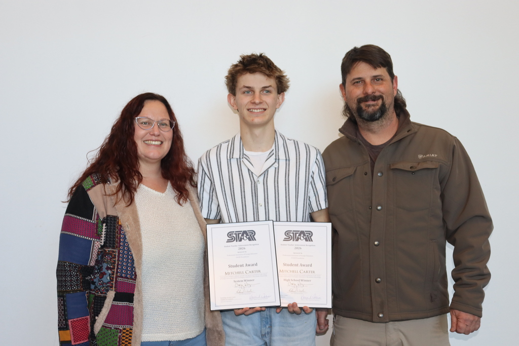 Mitchell Carter standing between two adults, smiling and holding his STAR Student Award certificates.
