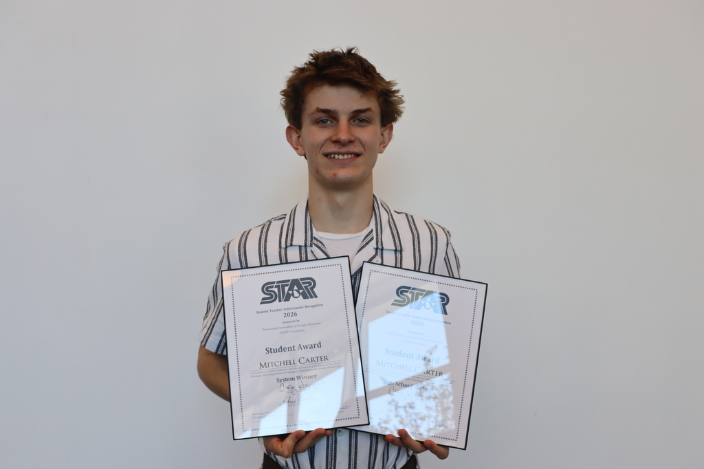 Young man smiling while holding two STAR Student Award certificates recognizing Mitchell Carter as a System Winner and High School Winner.