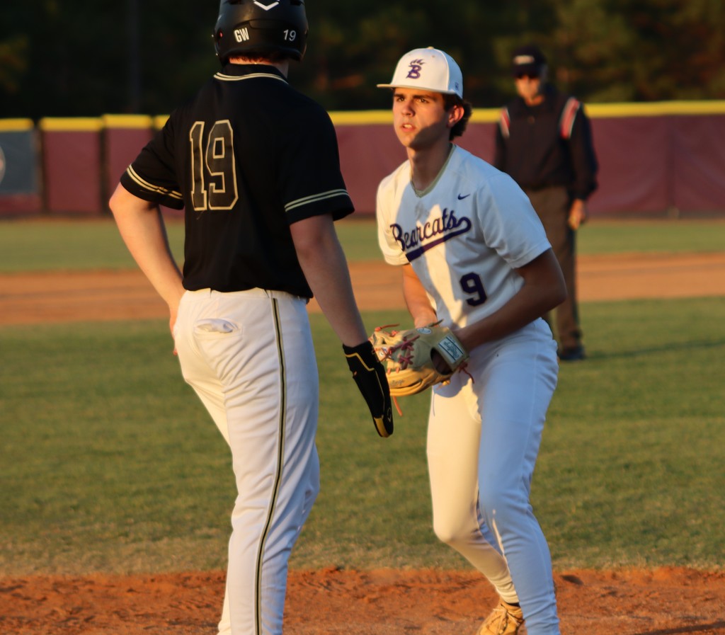 Infielder readies in a defensive stance as a runner leads off base.