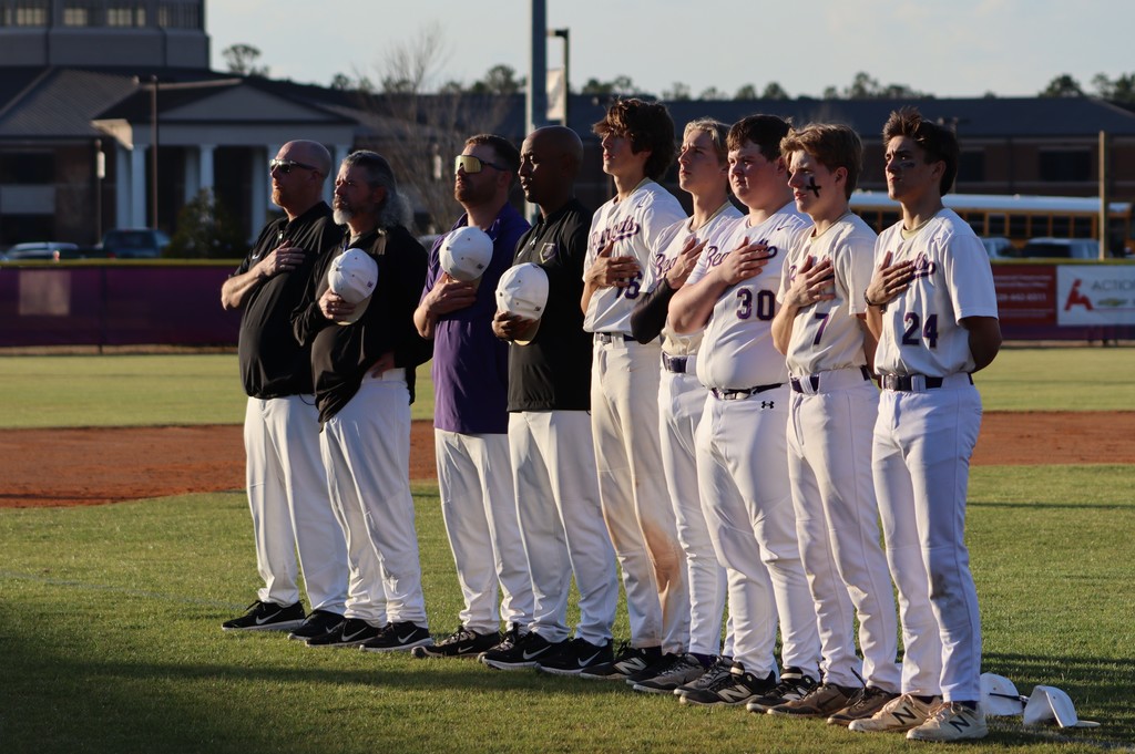 Players and coaches stand with hands over their hearts during the national anthem.
