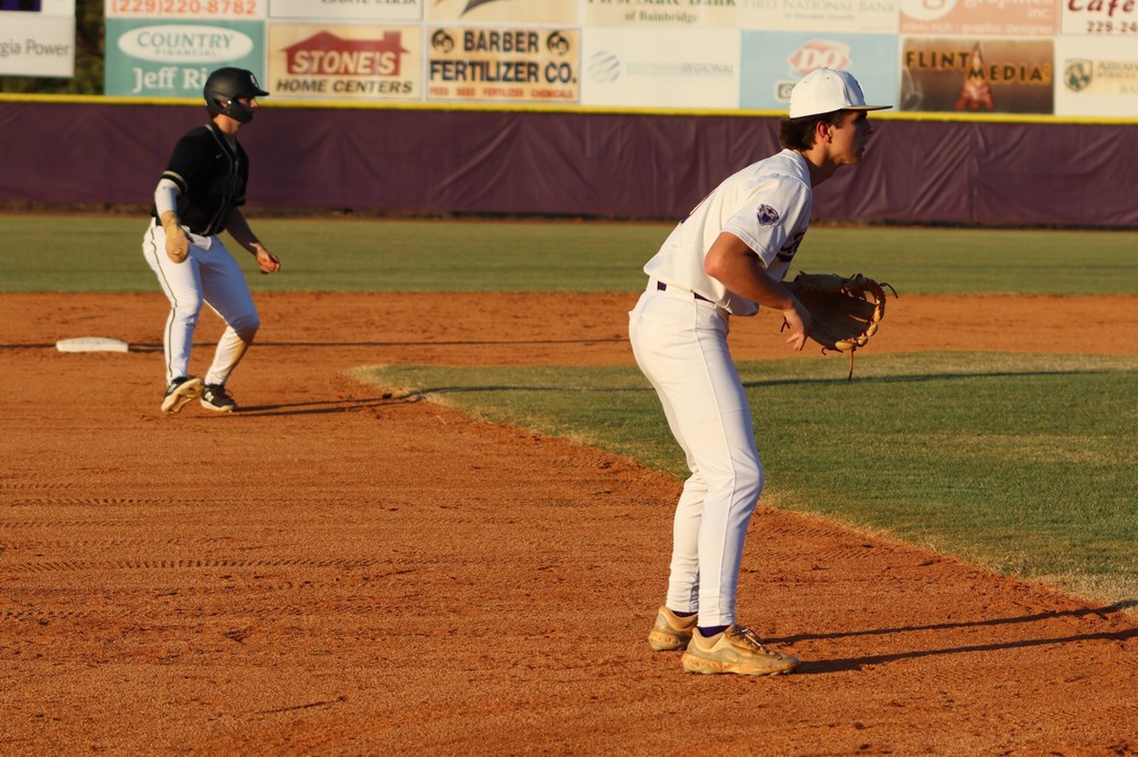 Infielder readies in a defensive stance as a runner leads off base.