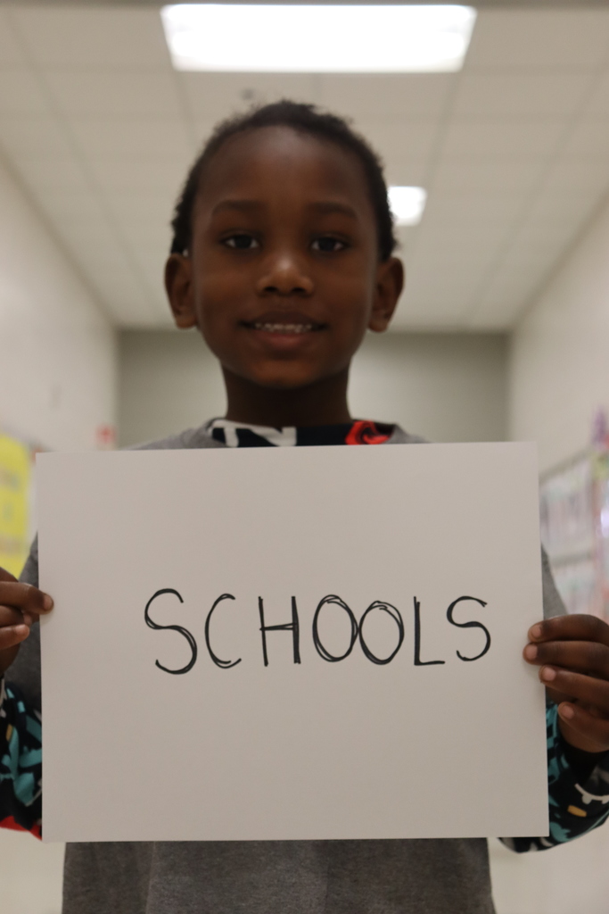 student smiling and holding a white sheet of paper that reads, "schools"