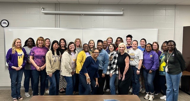 A group of school staff members gathered indoors at a school, smiling for a group photo.