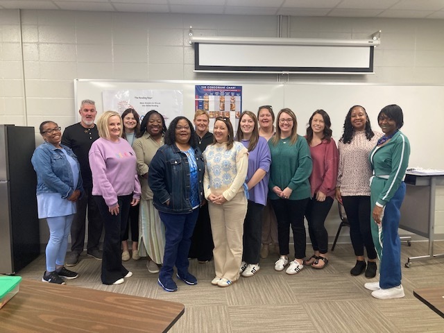 A group of school staff members gathered indoors at a school, smiling for a group photo.