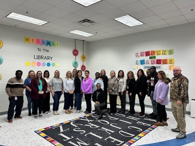 A group of school staff members gathered indoors at a school, smiling for a group photo.