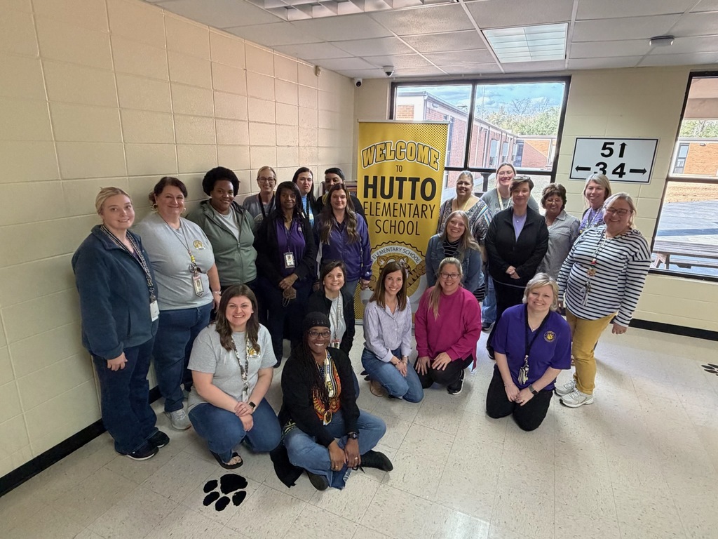 A group of school staff members gathered indoors at a school, smiling for a group photo.