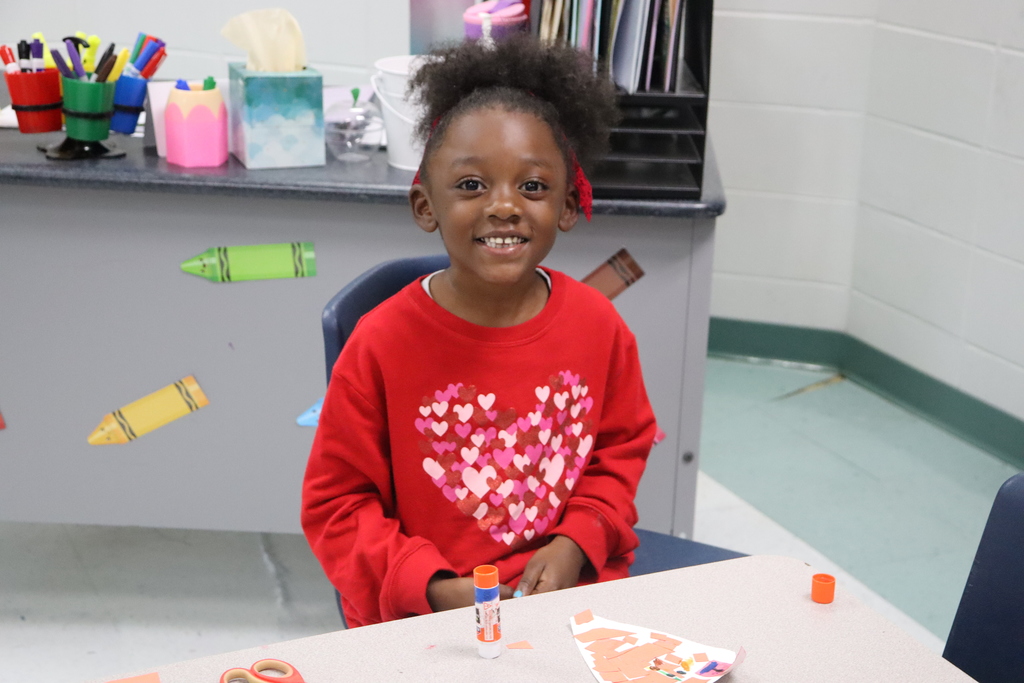 girl sits in front of table using a glue stick and smiling for a picture