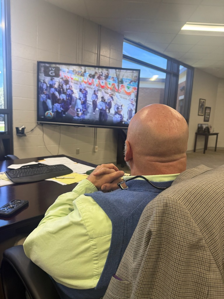 Superintendent watches the Bainbridge High School band marching in the NYC St. Patrick’s Day Parade on a TV from his office desk.