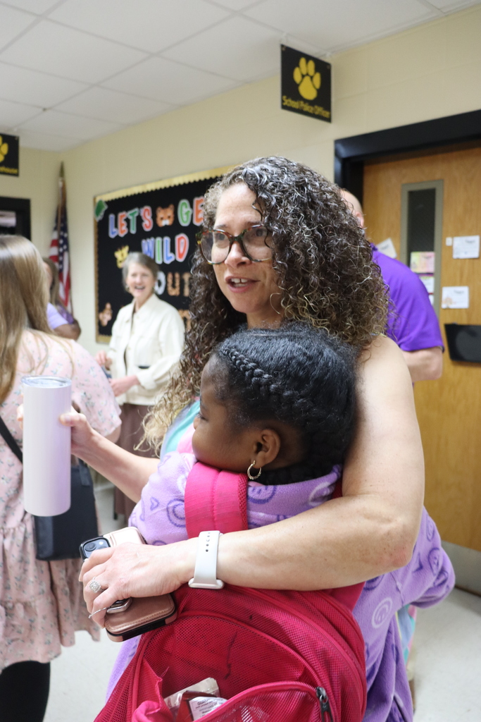 Staff member holds a student while talking with others during a teacher appreciation event.