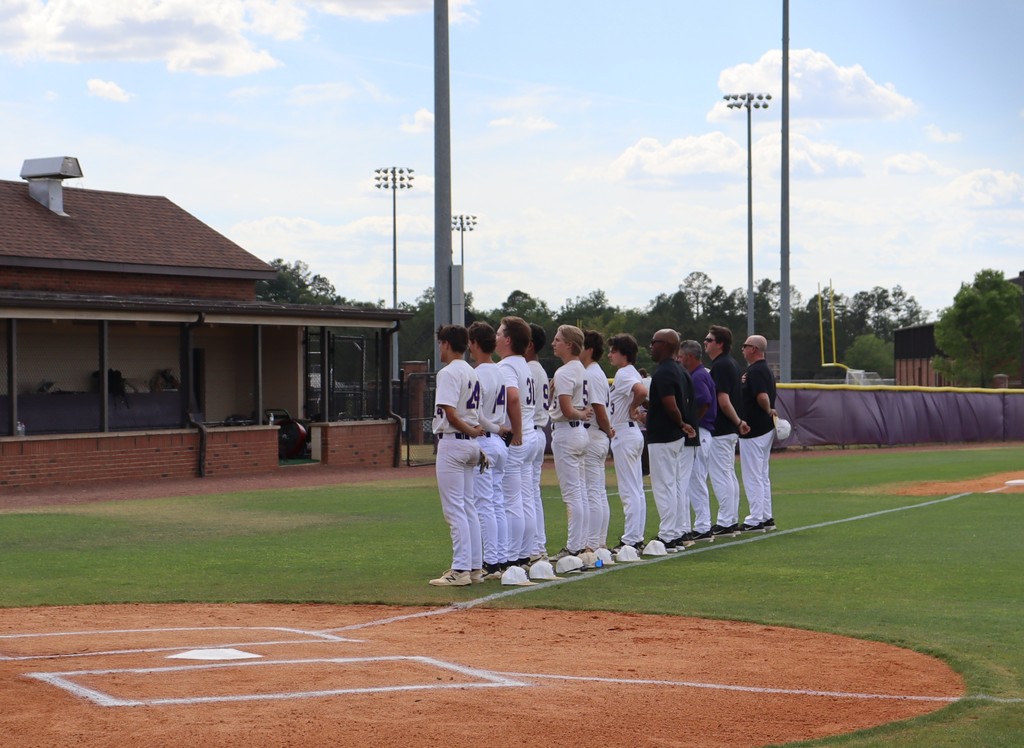 High school baseball game featuring Bainbridge Bearcats players in white uniforms fielding, pitching, catching, and running bases on a dirt and grass field, with a scoreboard, outfield fence signage, and spectators in the background.