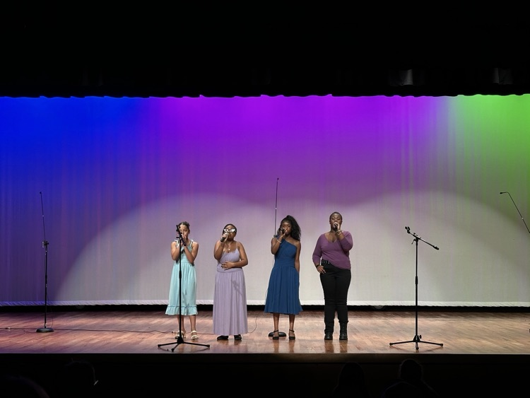 Four students perform in front of a lighted backdrop.