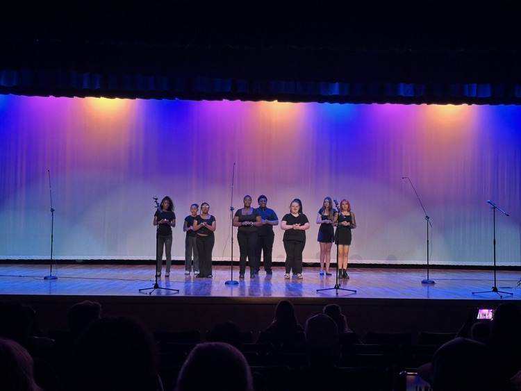 Several students perform in front of a lighted backdrop.