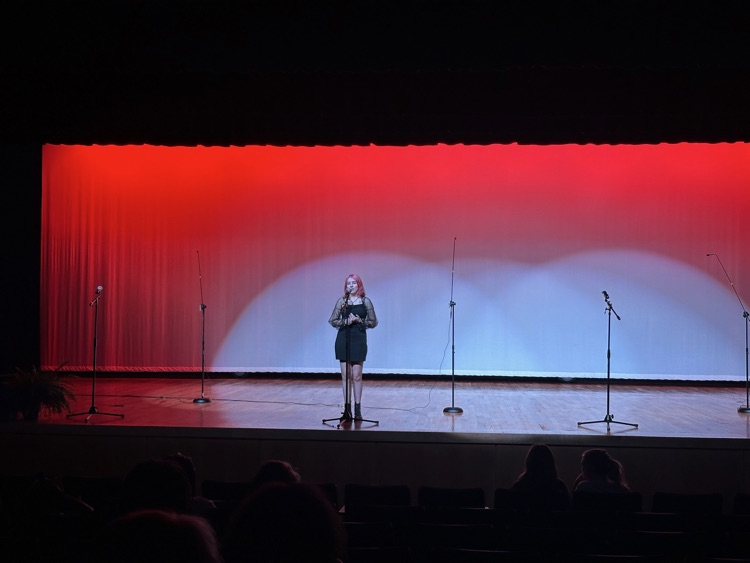 A student performs in front of a red lighted backdrop.