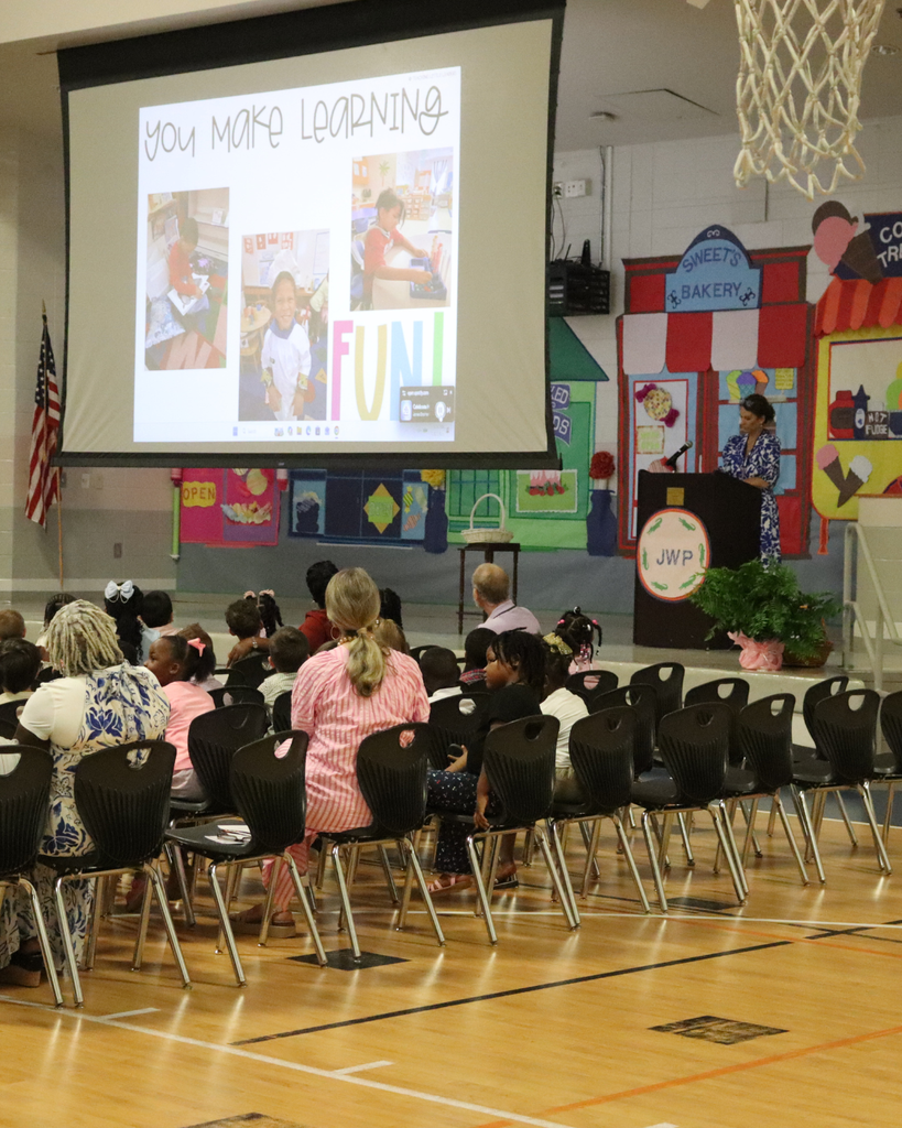 A teacher speaks at the podium during the JWP Pre-K awards ceremony as students and families watch from the audience.