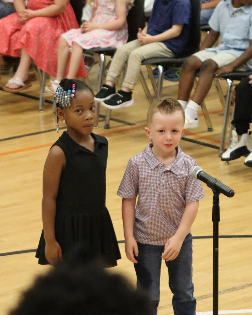 Two Pre-K students stand together at a microphone during the awards program presentation.