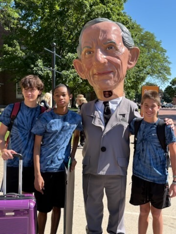 A series of photos shows three middle school students participating in a STEM and innovation event at a museum. The students explore interactive exhibits, including a flight simulator and historical automobile displays, while learning about engineering and technology. They examine informational exhibits, speak with event organizers and judges about STEM projects, and view a prototype backpack designed with ventilation and cooling features. Additional photos show the students receiving event materials, engaging in discussions about their project, and posing outdoors beside a large Abraham Lincoln mascot figure. The images capture hands-on learning, teamwork, problem-solving, and student engagement in science, technology, engineering, and innovation activities.