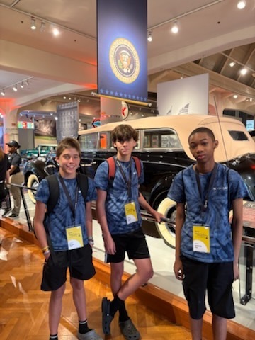 A series of photos shows three middle school students participating in a STEM and innovation event at a museum. The students explore interactive exhibits, including a flight simulator and historical automobile displays, while learning about engineering and technology. They examine informational exhibits, speak with event organizers and judges about STEM projects, and view a prototype backpack designed with ventilation and cooling features. Additional photos show the students receiving event materials, engaging in discussions about their project, and posing outdoors beside a large Abraham Lincoln mascot figure. The images capture hands-on learning, teamwork, problem-solving, and student engagement in science, technology, engineering, and innovation activities.