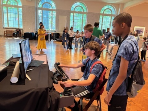 A series of photos shows three middle school students participating in a STEM and innovation event at a museum. The students explore interactive exhibits, including a flight simulator and historical automobile displays, while learning about engineering and technology. They examine informational exhibits, speak with event organizers and judges about STEM projects, and view a prototype backpack designed with ventilation and cooling features. Additional photos show the students receiving event materials, engaging in discussions about their project, and posing outdoors beside a large Abraham Lincoln mascot figure. The images capture hands-on learning, teamwork, problem-solving, and student engagement in science, technology, engineering, and innovation activities.