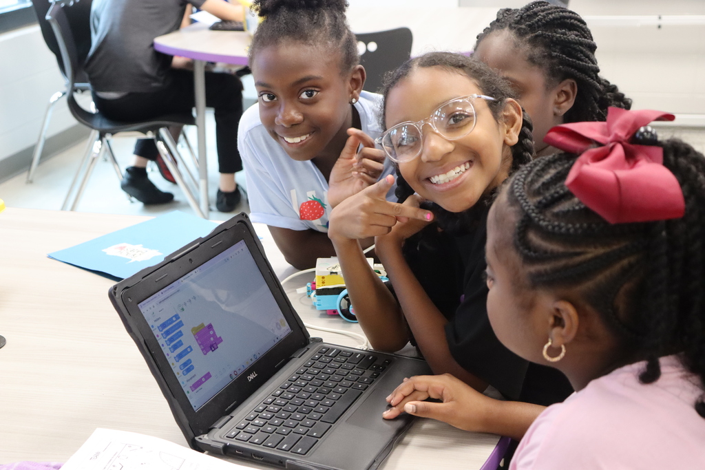 Students smile together while using block coding to program a robotics activity during Summer STEM Camp.
