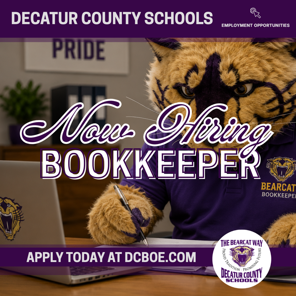 Bearcat mascot in a purple polo working at a desk with a calculator, paperwork, and laptop in a bookkeeping office.