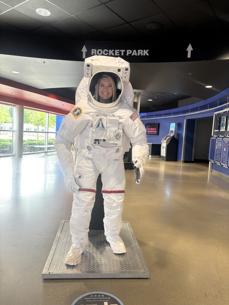 A smiling woman poses in a NASA spacesuit display at the U.S. Space & Rocket Center.