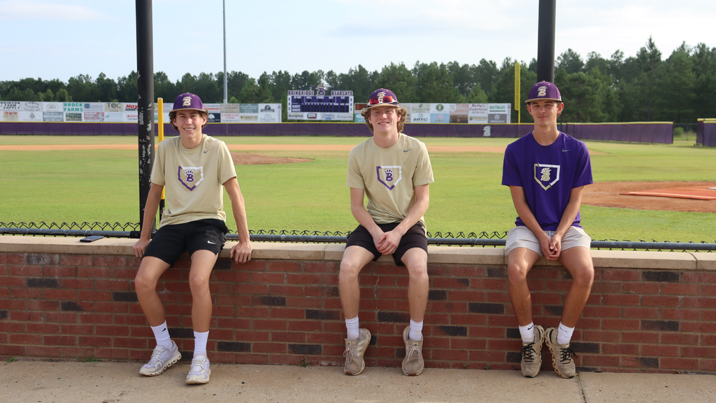 Three Bearcat baseball players sit together near the field.