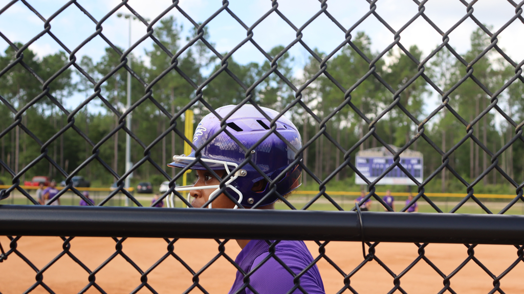 Softball player watches the field from behind the dugout fence.