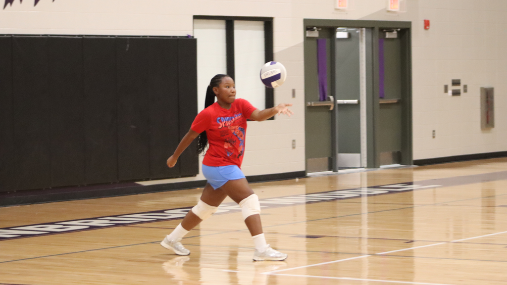 Volleyball player practices serving in the BMS gym.