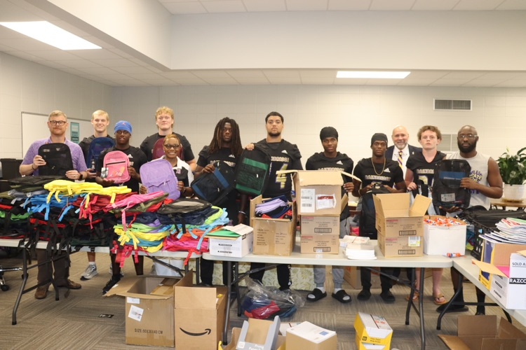 BHS football players pose for a picture with score staff in from of tables full of school supplies